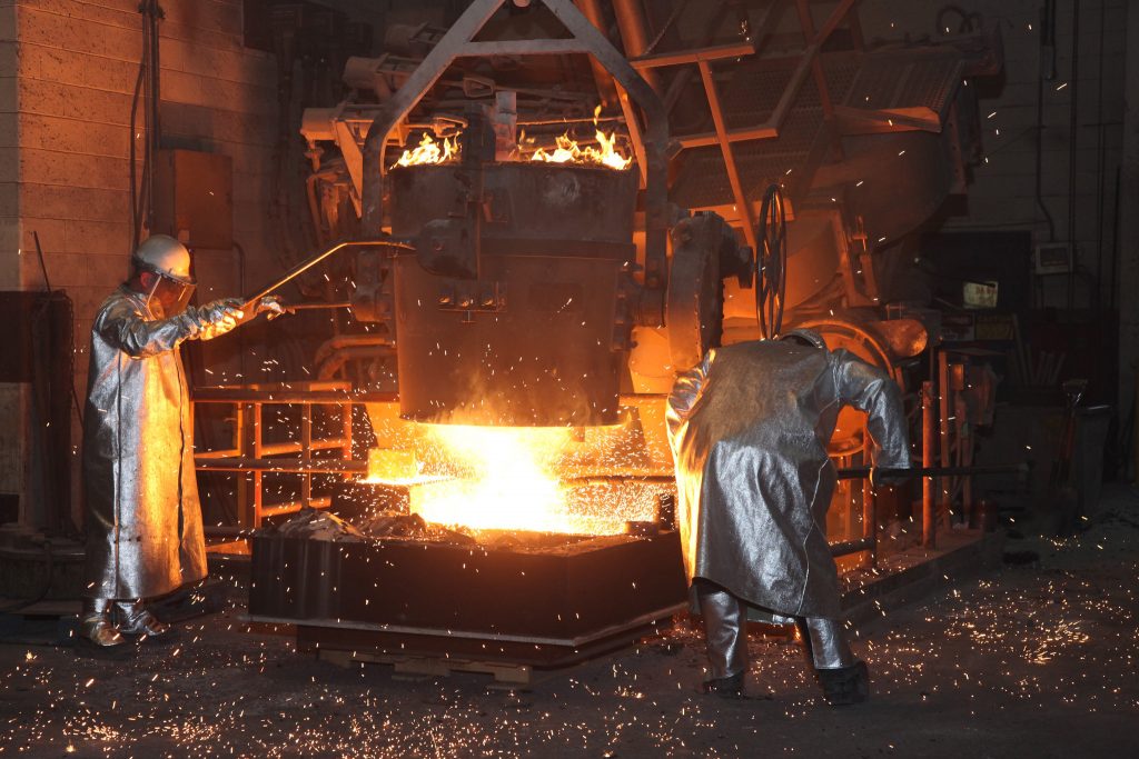 Giesserei, Arbeiter giessen Stahl in eine Sandform. Sand solcher Formen kann durch die Giessereiltsandverwertung nachhaltig entsorgt werden.